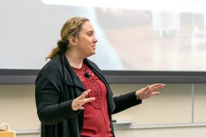 Holly Strauss speaks to attendees in front of slide show
